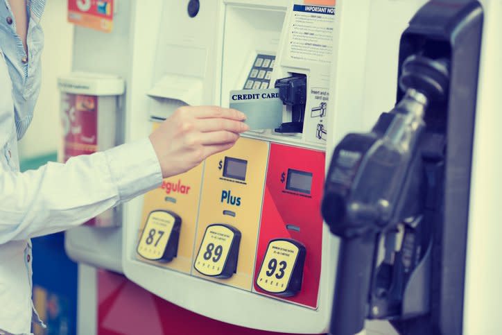 A hand placing a credit card into a gas pump card reader.