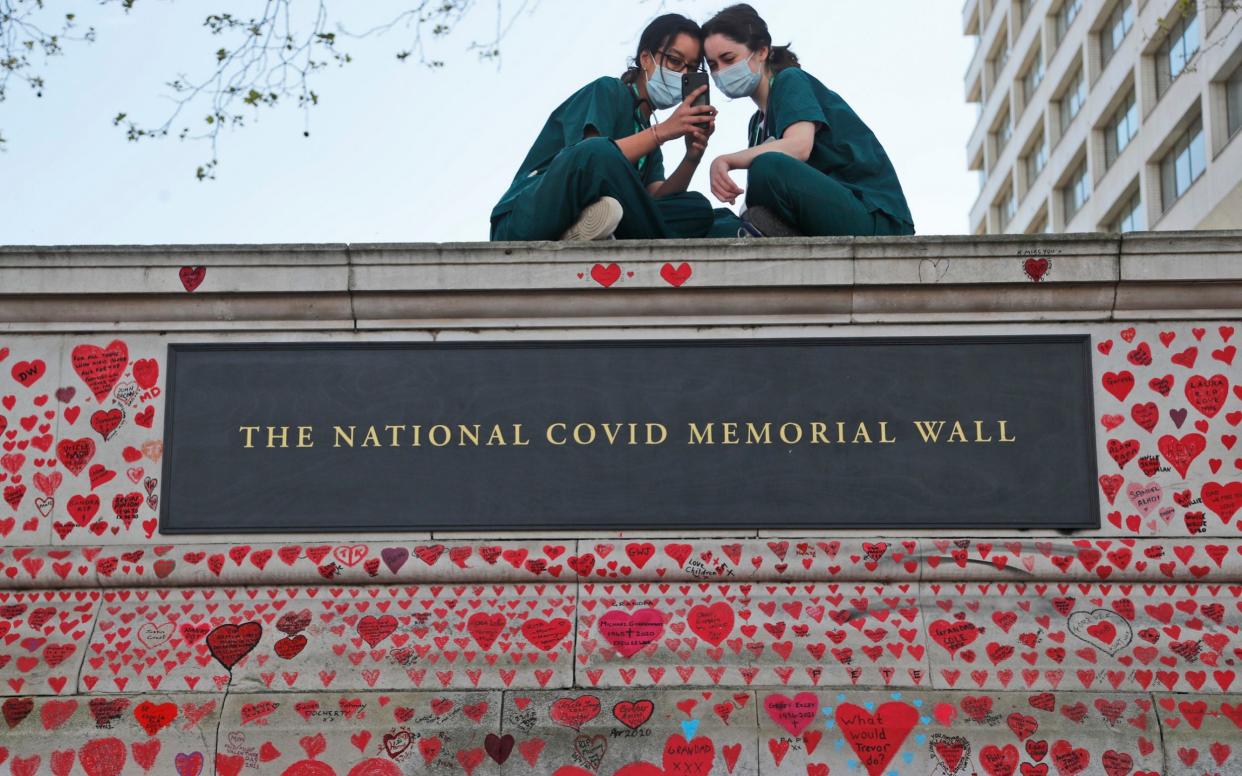 Nurses from the nearby St Thomas' hospital sit atop the National Covid Memorial Wall in London.  -  Frank Augstein/AP