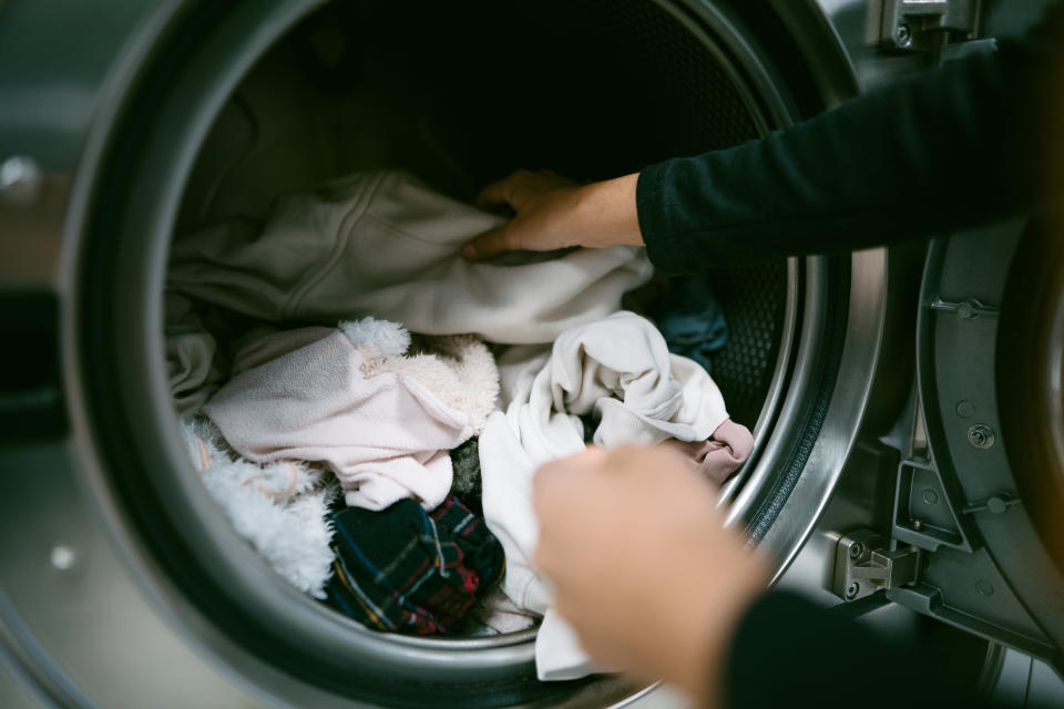 Young woman hands putting her dirty clothes in the washing machine in a laundromat. Self service laundry