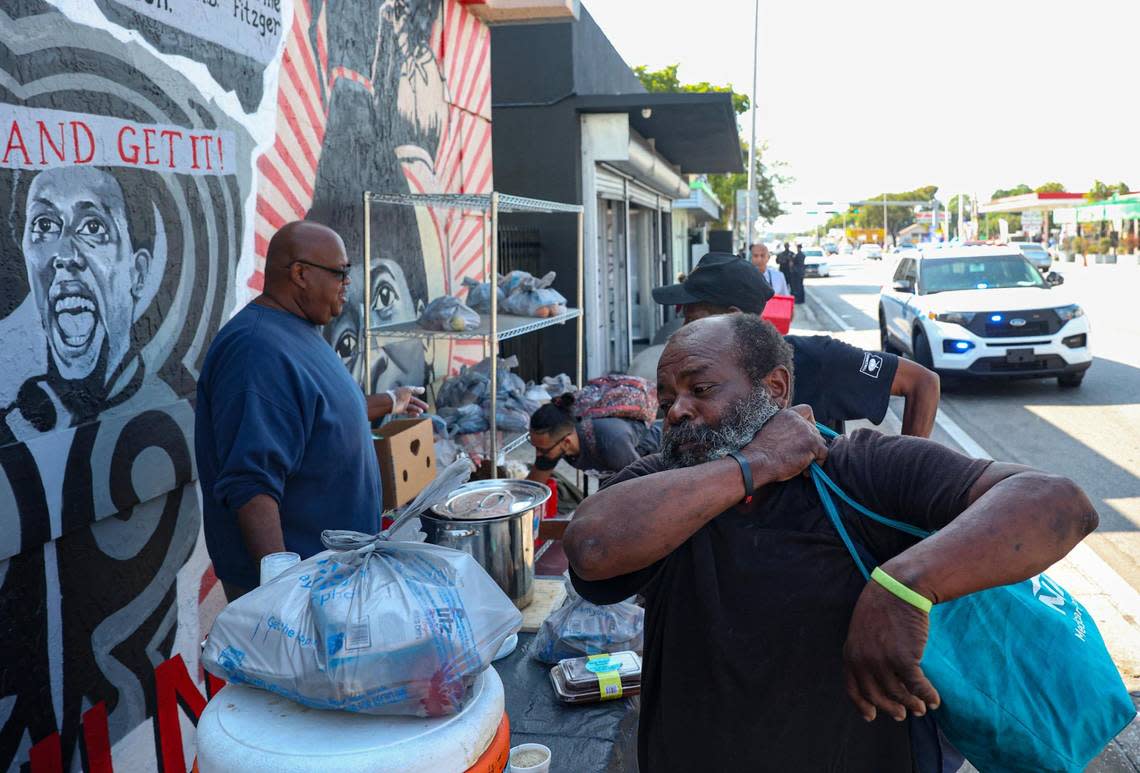 Larry Grubbs, center, gathers food from the station the Village FREEdge set up down the street to feed the community while it gets evicted, back of the photo, on Monday, March 6, 2023, in Liberty City. City of Miami Police and Miami-Dade Police showed up with the Gator Investments landlord and the eviction papers around 8:45 a.m. as the pantry was getting ready to serve the morning meal.