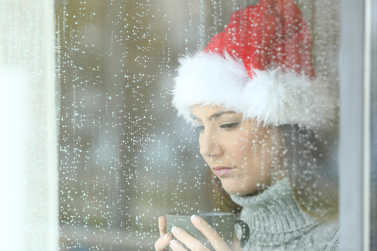 Sad woman in christmas looking down through a windos in a rainy day