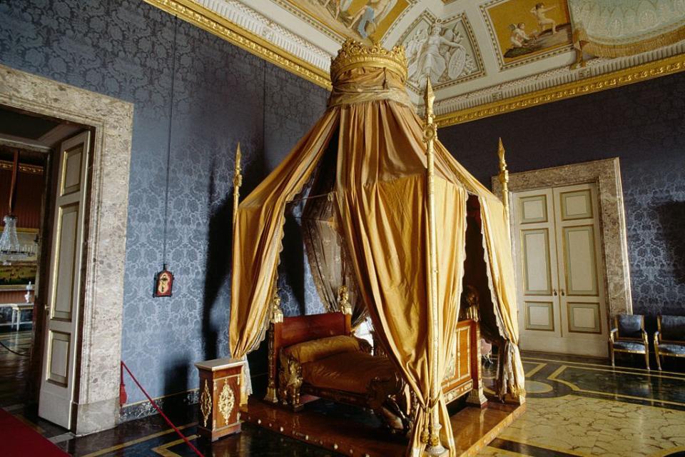 <p>The former Italian royal residence is the world's largest palace, and this stunning bedroom of King Francis II of Bourbon is a beautiful example of a <em>lit à la polonaise </em>bed. The style was named for King Louis XV's Polish queen but was first used in France. The golden cascading fabric of this Italian palace shines against the deep blue upholstered walls. <br></p>