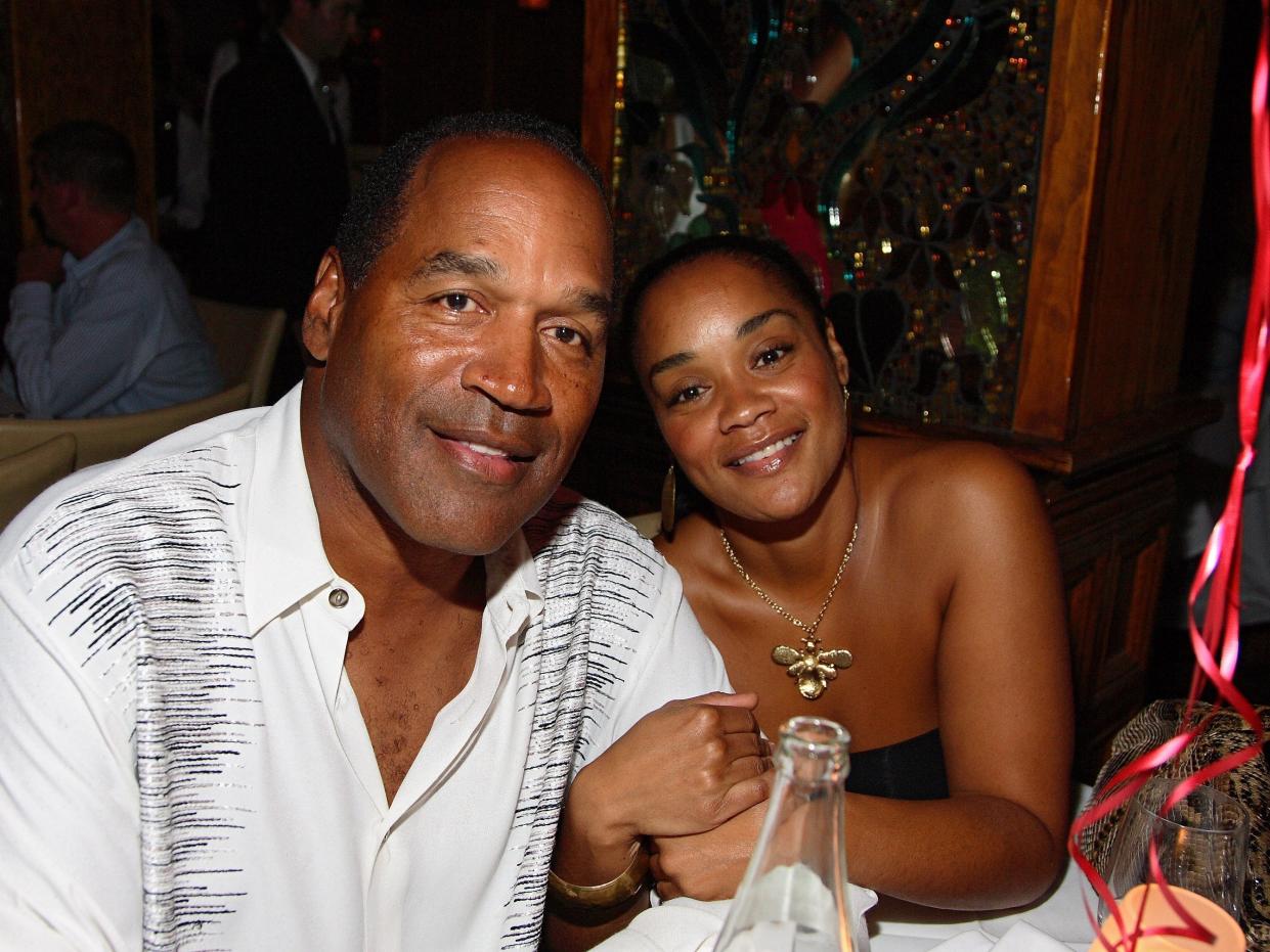 oj simpson and his daughter arnelle simpson, smiling and posing together while sitting at a table. there are ribbons visible in the corner of the frame