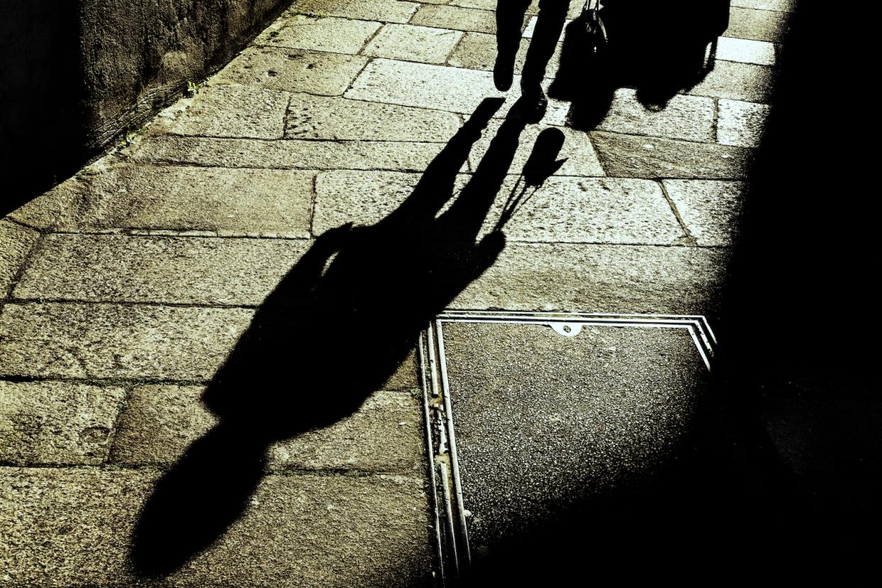 A shadow of a person walking at a dark alleyway, signifying danger.