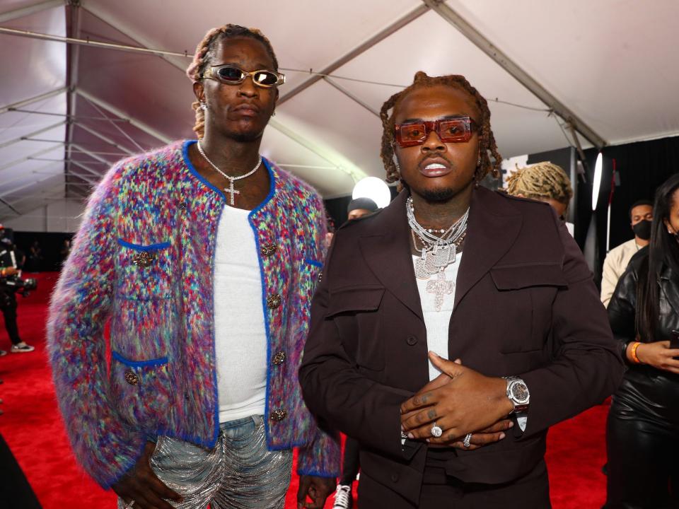 Young Thug, in a multicolored cardigan and sunglasses, poses for photos on the red carpet with Gunna, in a brown jacket and sunglasses.