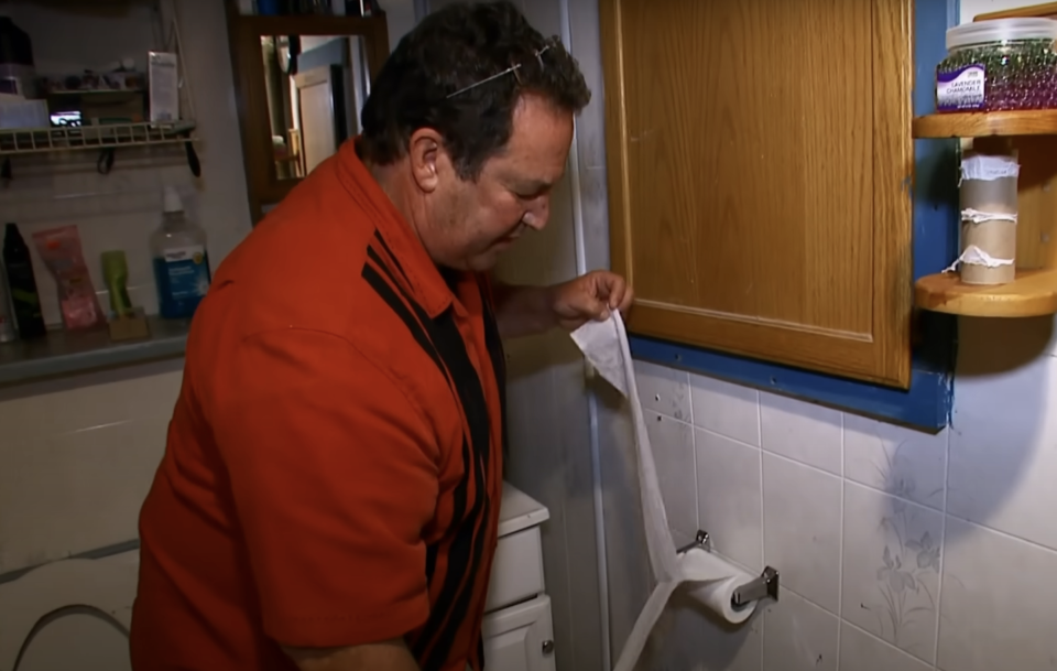 Man examining a towel in a kitchen setting, possibly from a scene in a TV show or movie