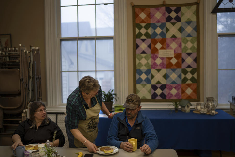 Volunteer Kathy Miller, center, serves breakfast to Travis Godfrey, right, and Donna Sherlaw at the United Community Church in Morristown, Vt., Wednesday, March 6, 2024. Miller once testified before Congress about the impact of credit card fees. Back then, she believed that little people could have a voice in national politics. But these days, she says, Washington has gotten away from the basics. Too big, she says. Too messed up. Tilted off its axis. (AP Photo/David Goldman)