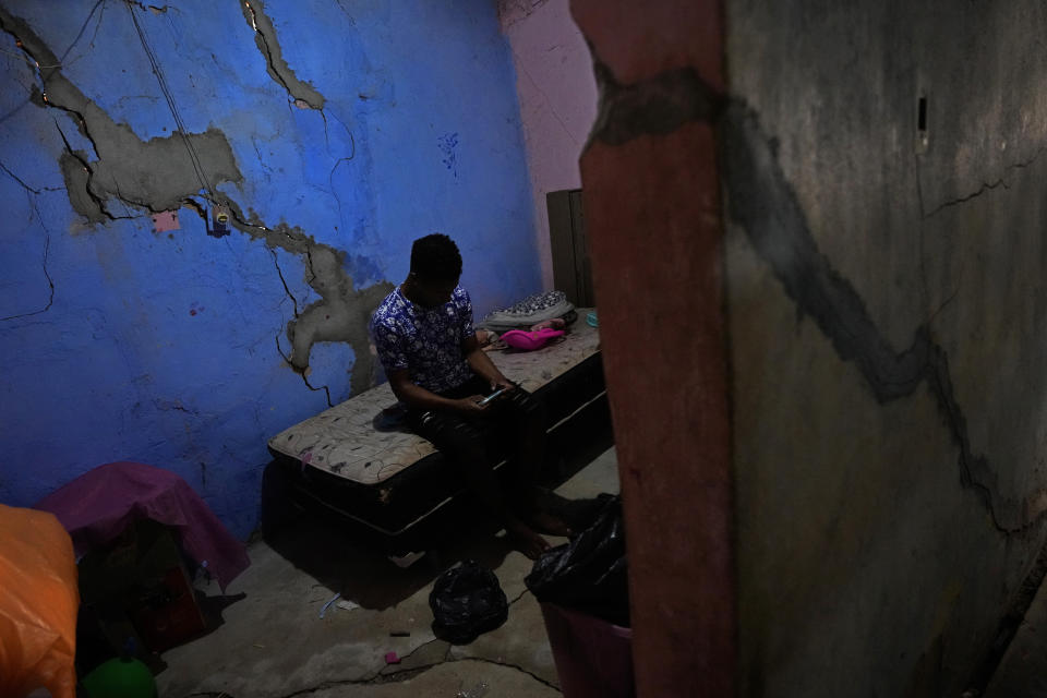 Israel Oliveira checks his mobile phone as he sits on a bed inside his damaged home in the Bom Parto neighborhood of Maceio, Alagoas state, Brazil, Monday, March 7, 2022. Oliveira´s home has been damaged by ground subsidence caused by the Braskem mine that has forced more than 55 thousand people from their homes in Maceio. (AP Photo/Eraldo Peres)