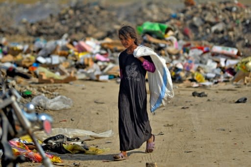 An Iraqi girl carrying a bag walks amidst piles of rubbish in a landfill in Diwaniyah, south of the capital Baghdad