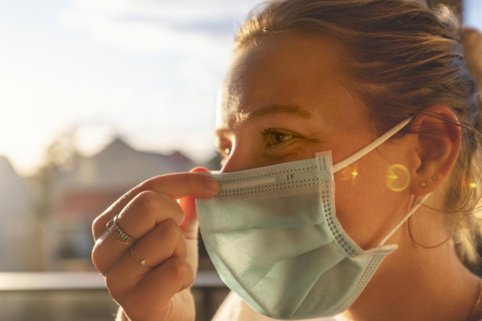 woman touching the nose of her surgical face mask while outside