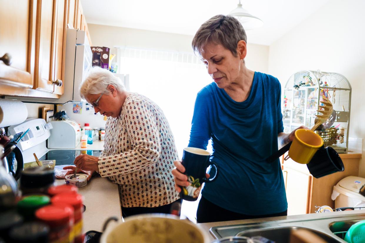 Marlene Mears, right, puts away dishes while Becky Miller, left, prepares food in their kitchen in Longmont, Colo.