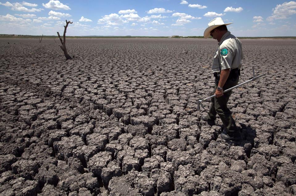 In this Aug 3, 2011 file photo, Texas State Park police officer Thomas Bigham walks across the cracked lake bed of O.C. Fisher Lake, in San Angelo, Texas.