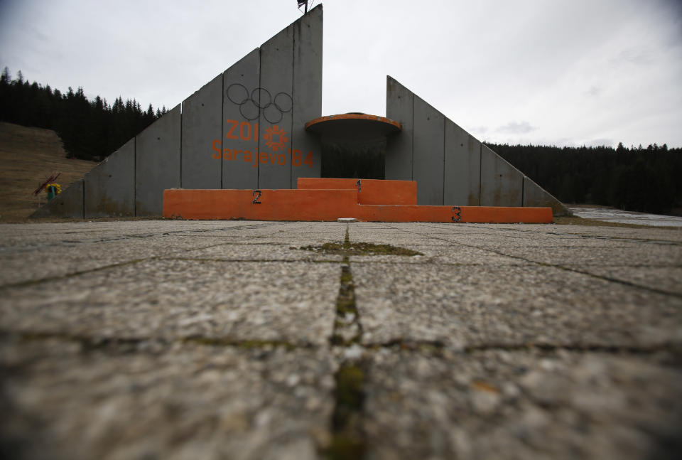 In this picture taken on Friday, Feb. 21, 2014, a concrete podium for winners with the text "Winter Olympic Games 1984" stands abandoned near jumping hills at Mt. Igman near the Bosnian capital of Sarajevo. Wartime destruction and negligence have turned most of Sarajevo's 1984 Winter Olympic venues into painful reminders of the city's golden times. The world came together in the former Yugoslavia in 1984 after the West had boycotted the 1980 Olympics in Moscow and Russia boycotted the 1984 Summer Games in Los Angeles. Just eight years later, the bobsleigh and luge track on Mount Trbevic was turned into an artillery position from which Bosnian Serbs pounded the city for almost four years. Today, the abandoned concrete construction looks like a skeleton littered with graffiti. (AP Photo/Amel Emric)