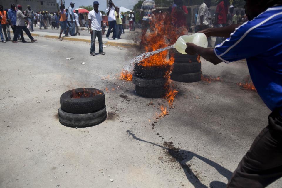 A protester throws gasoline to help ignite tires during a protest against President Michel Martelly's government in Port-au-Prince, Haiti, Tuesday April 15, 2014. Those demonstrating called for the resignation of Martelly. (AP Photo/Dieu Nalio Chery)