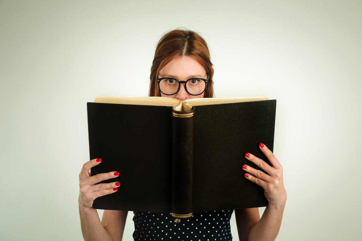 Young woman holding big thick book, looking at camera