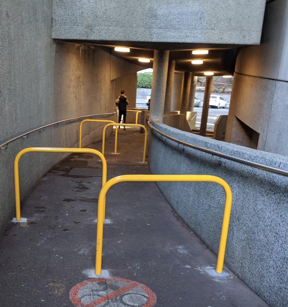 The pathway near Hamer Hall can be seen with as many as five yellow metal barriers impeding the path.