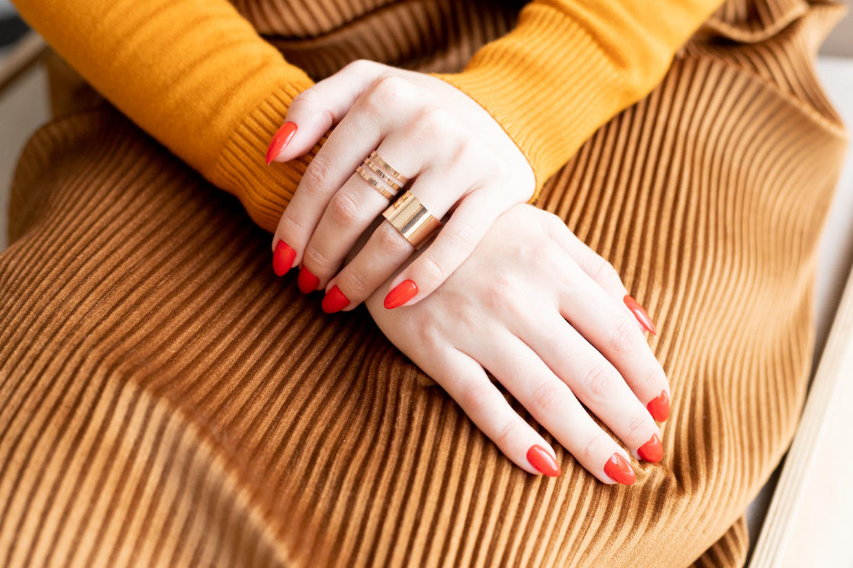 The Young woman's hands with Red manicure and gold rings are on her lap