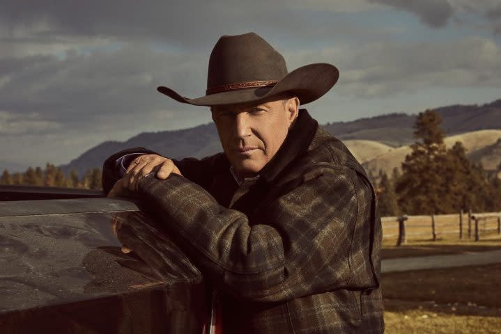 Kevin Costner rests his arms up against a fence.