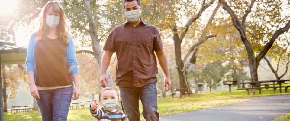 Happy Mixed Race Ethnic Family Walking In The Park Wearing Medical Face Mask.