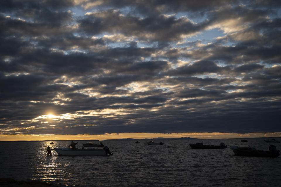 Two hunters prepare their boat for seal hunting in the morning as the sun peaks through the clouds in Shishmaref, Alaska, Monday, Oct. 3, 2022. Shishmaref sits on the small island of Sarichef -- just a quarter of a mile wide and about three miles long. Only about half of it is habitable, but hundreds of feet of shore have been lost in past decades. (AP Photo/Jae C. Hong)