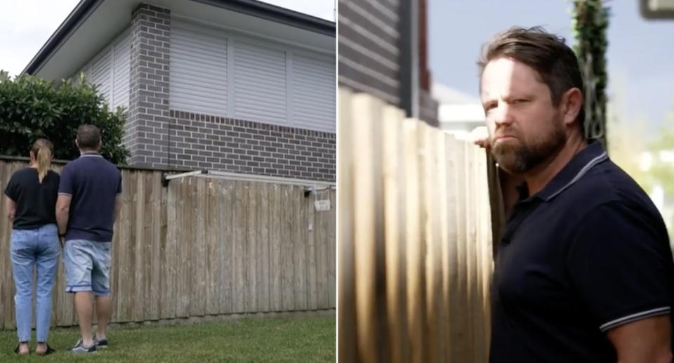 Jay and his wife Kirsty Hall standing in their backyard looking at the fence. Jay standing at the fence with his hand on top of it, scowling expression.