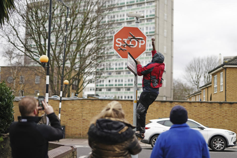 A person removes a piece of art work by Banksy, which shows what looks like three drones on a traffic stop sign, which was unveiled at the intersection of Southampton Way and Commercial Way in Peckham, south east London, Friday Dec. 22, 2023. (Aaron Chown/PA via AP)