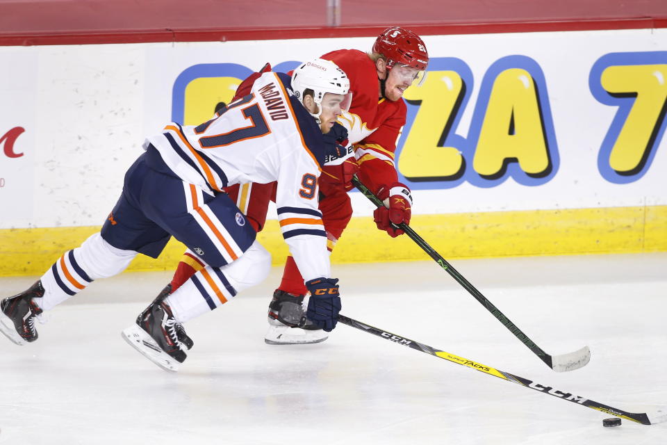 Edmonton Oilers' Connor McDavid, left, and Calgary Flames' Joakim Nordstrom reach for the puck during the first period of an NHL hockey game Saturday, April 10, 2021, in Calgary, Alberta. (Larry MacDougal/The Canadian Press via AP)