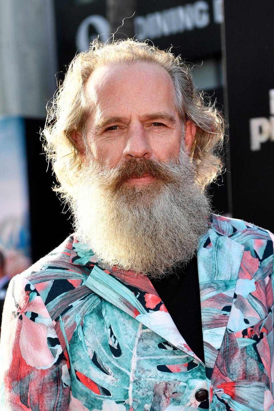 Neil Sandilands with a long beard in a floral blazer posing for a photo at the premiere for the Kingdom of the Planet of the Apes