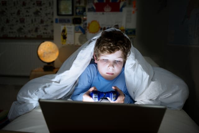 Young boy 10 years old playing on his computer late at night. Illustrating the idea that children are too tired for school in th