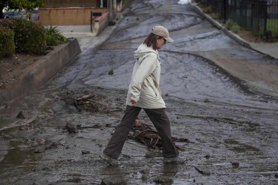 A woman walks over the mud and debris at the corner of Sierra Madre Avenue and Highcrest Road along the hillside in Glendora, Calif. on Saturday, March 1, 2014. A burst of heavy showers before dawn Saturday impacted wildfire-scarred mountainsides above foothill suburbs east of Los Angeles, causing another round of mud and debris flows in the city of Glendora. (AP Photo/Ringo H.W. Chiu)