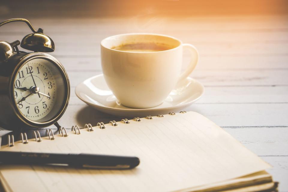 cup of hot coffee ,clock,notebook and pen on wooden table