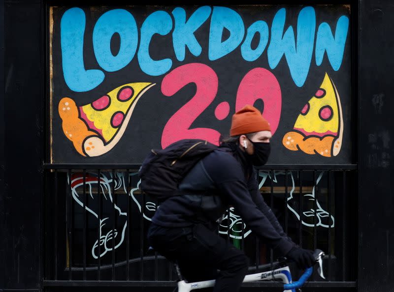 A man cycles past a mural on the boarded up window of a closed pizza restaurant in Manchester