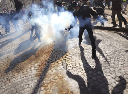 A protester throws back a tear gas canister as they clash with French riot police during a demonstration by the "yellow vests" movement in Paris, France, March 16, 2019. REUTERS/Philippe Wojazer