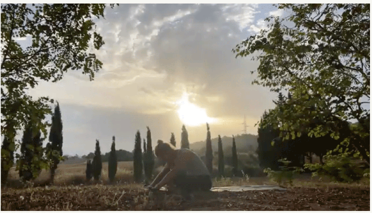 Woman seated cross-legged on her yoga mat outdoors at sunrise