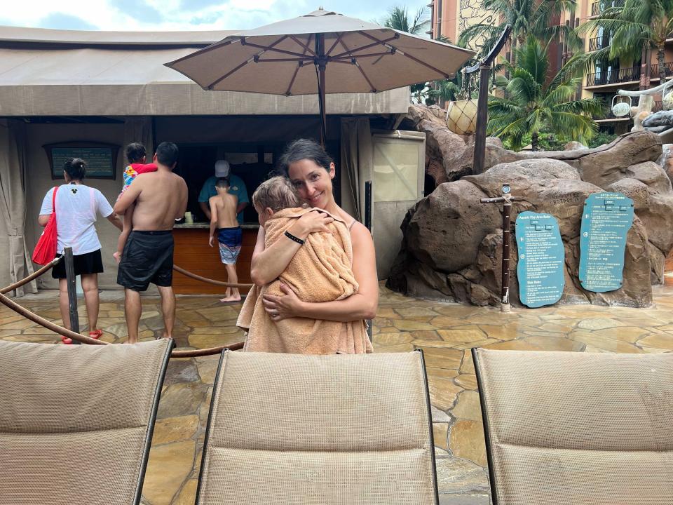 A woman holding her baby wrapped in a towel in a pool area.