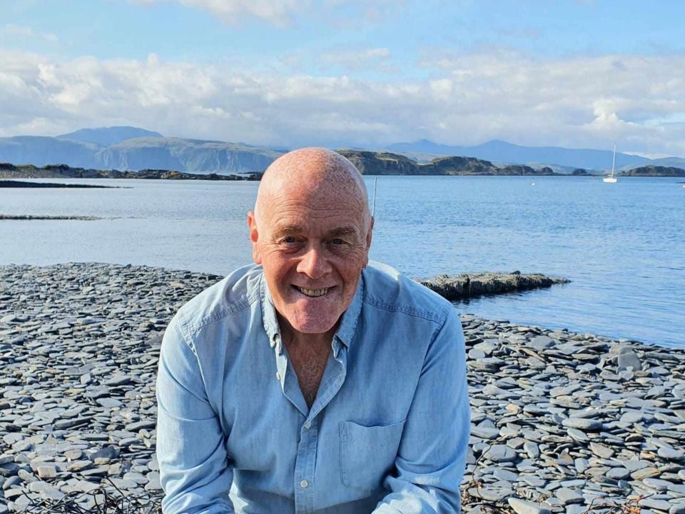 Melville smiling in front of a slate beach.