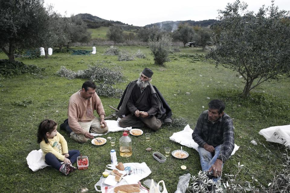 From left to right, Asimina Nikolopoulou, Tasos Nikolopoulos, Greek Orthodox Priest Dimitris Vlasopoulos, and Yiannis Nikolopoulos, have a picnic in an olive grove in Kalo Pedi village, about 335 kilometers (210 miles) west of Athens, Greece on Friday, Nov. 29, 2013. Widespread ownership of olive groves among Greeks has helped maintain supplies to households as they struggle through a sixth year of recession. (AP Photo/Petros Giannakouris)