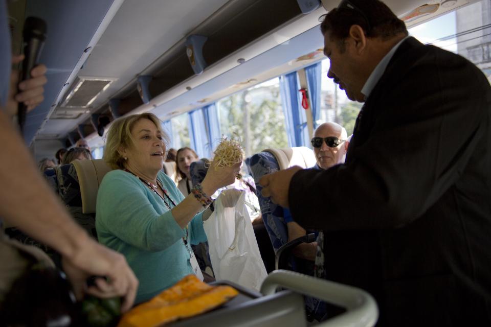 In this Jan. 23, 2014 photo, Ellen Landsberger a tourists from New York, traveling in the "people-to-people" program shows her tour bus driver what she bought in a Cuban agricultural market in Havana, Cuba. Two and a half years after the program was reinstated, a survey shared exclusively with The Associated Press suggests the trips are not only improving Cubans’ views of Americans. They are also changing U.S. travelers' opinions of the Caribbean nation for the better. (AP Photo/Ramon Espinosa)