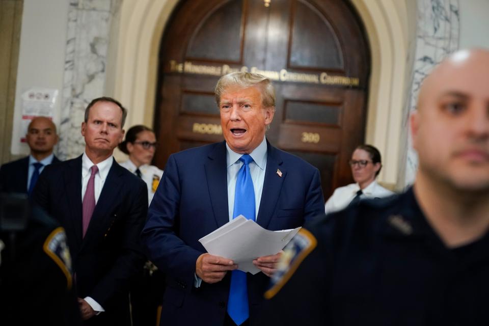 Donald Trump speaking outside a courtroom, holding a piece of paper.