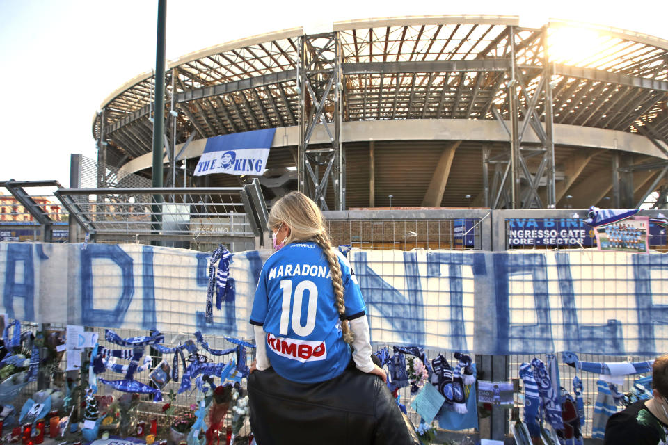 A girl sits on a man's shoulders as she looks at gadgets and memorabilia commemorating soccer legend Diego Maradona outside the San Paolo stadium, in Naples, southern Italy, Thursday, Nov. 26, 2020. Maradona died Wednesday, Nov. 25, 2020 in Buenos Aires. (AP Photo/Alessandra Tarantino)