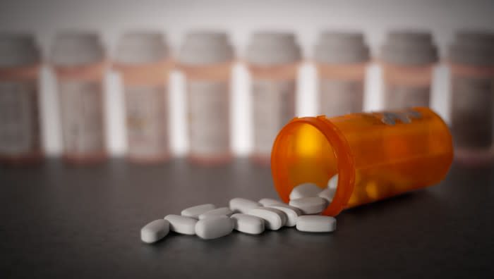 Pills spilled from a pill bottle with other pill bottles in the background