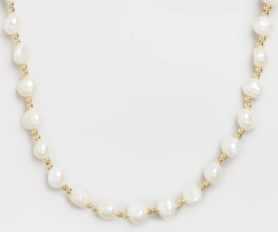 A white pearl and gold chain necklace against a white background.