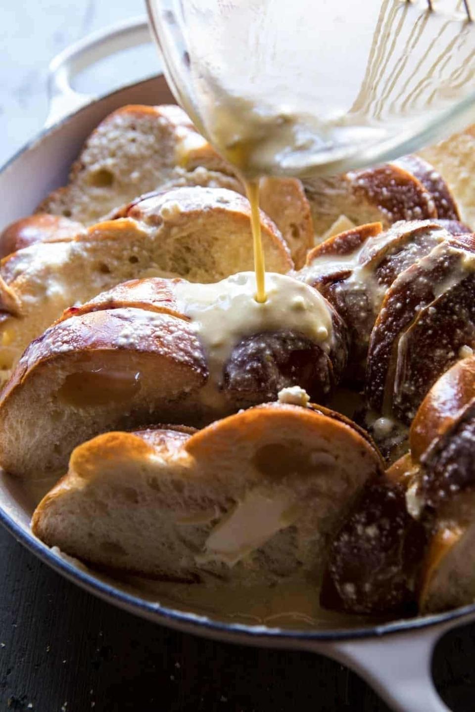 Close-up of a dish featuring sliced bread, with a creamy sauce being poured over it, likely preparing a bread pudding or French toast casserole