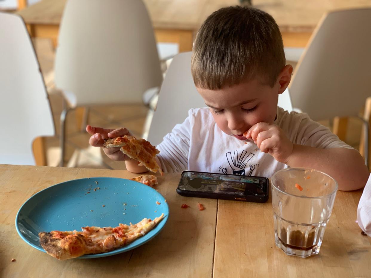 kid on phone eating pizza