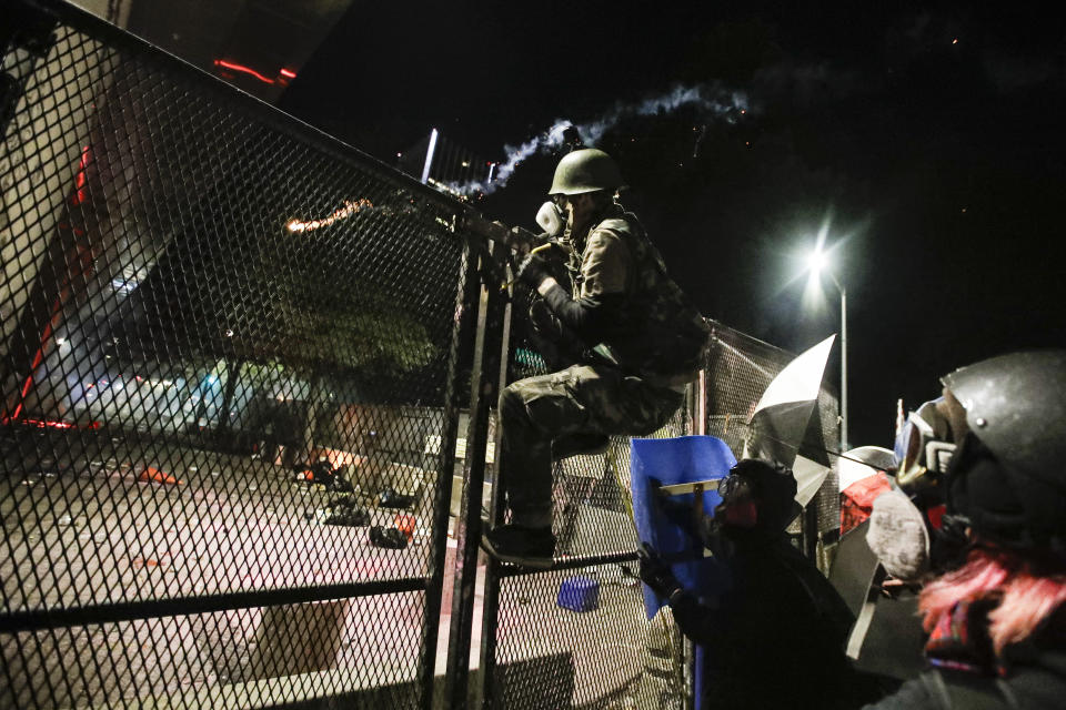 A demonstrator tries to climb over a fence during a Black Lives Matter protest at the Mark O. Hatfield U.S. Courthouse, Sunday, July 26, 2020, in Portland, Ore. On the streets of Portland, a strange armed conflict unfolds night after night. It is raw, frightening and painful on both sides of an iron fence separating the protesters on the outside and federal agents guarding a courthouse inside. This weekend, journalists for The Associated Press spent the weekend both outside, with the protesters, and inside the courthouse, with the federal agents, documenting the fight that has become an unlikely centerpiece of the protest movement gripping America. (AP Photo/Marcio Jose Sanchez)