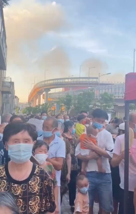 中國網友拍到重慶居民在高溫達40度的環境下排隊做核酸檢測，後方是野火產生的濃煙。   圖: 翻攝自 小艾EYE  微博