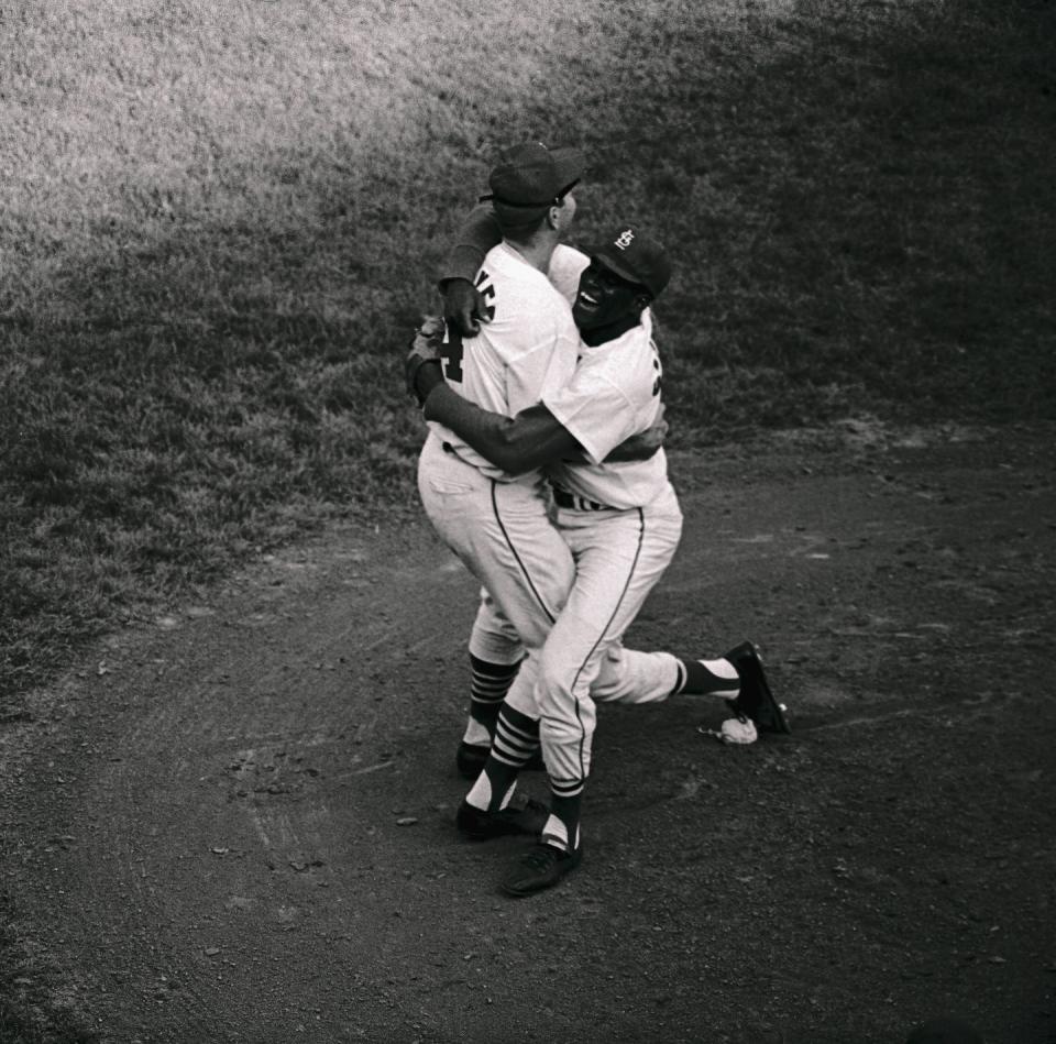 two baseball players hug and smile on the mound of a baseball field