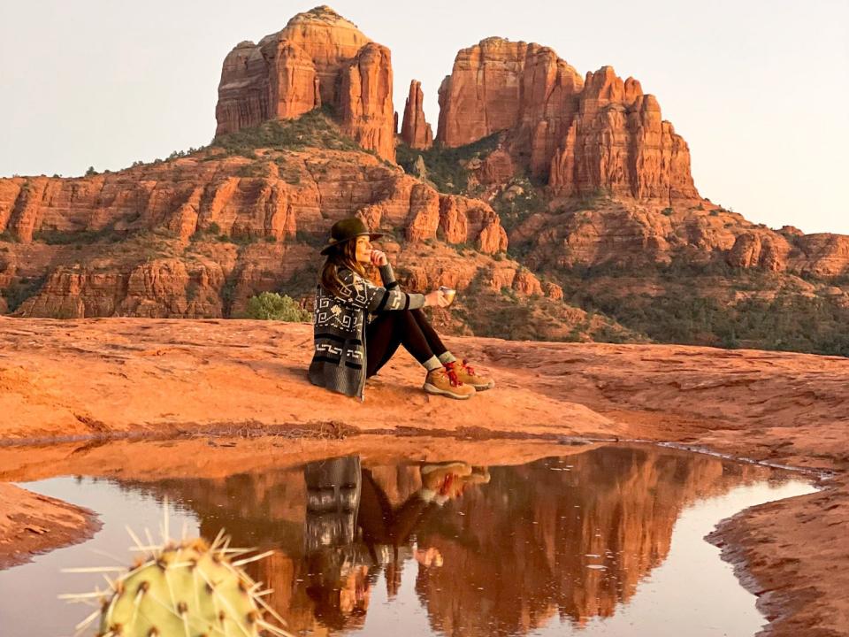 Emily sits on red rock in front of vast rock structures and in front of a small body of water.