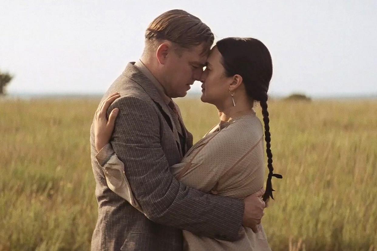 DiCaprio and Gladstone as Ernest and Mollie embrace in a scenic wheat field. 