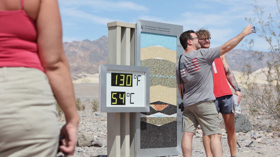 Tourists stand next to an unofficial heat reading at Furnace Creek Visitor Center during a heat wave in Death Valley National Park. - Ronda Churchill/AFP/Getty Images